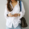 Person wearing a white shirt and blue jeans, holding a phone and a brown handbag.