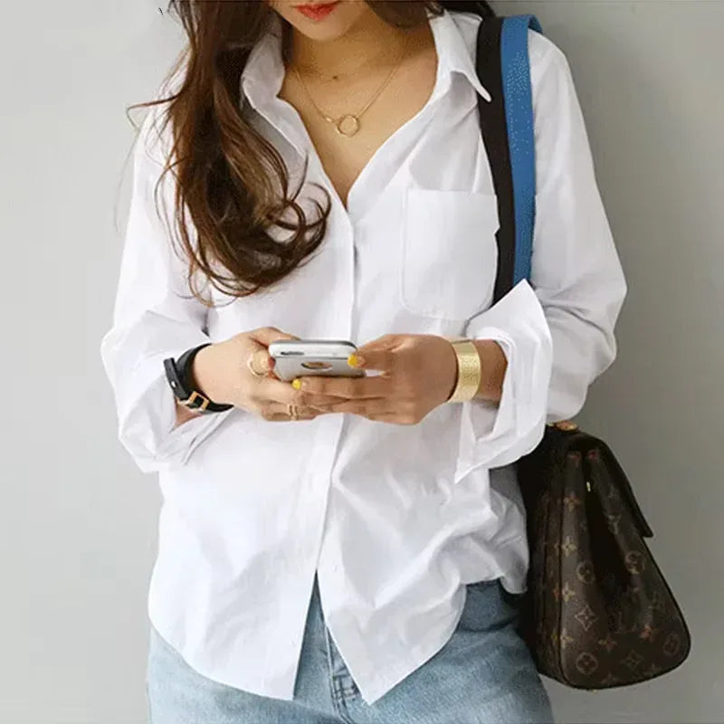 Person wearing a white shirt and blue jeans, holding a phone and a brown handbag.