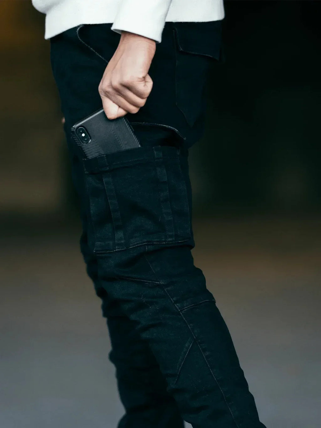 Person wearing dark pants with a phone in the pocket against a blurred background