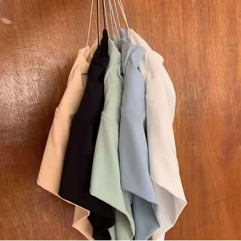 Five shirts in beige, black, green, blue, and pink hanging on a wooden surface.