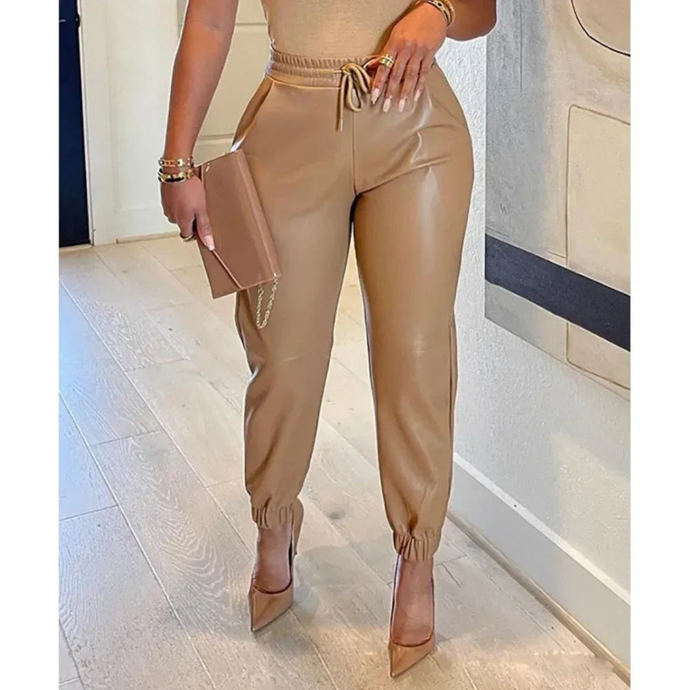 Person wearing beige pants and high heels, holding a clutch in an indoor setting.