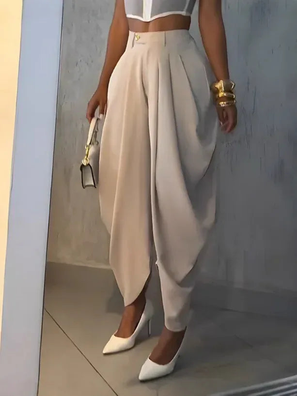 Person wearing a white top and beige drape pants with white shoes, holding a gold clutch.