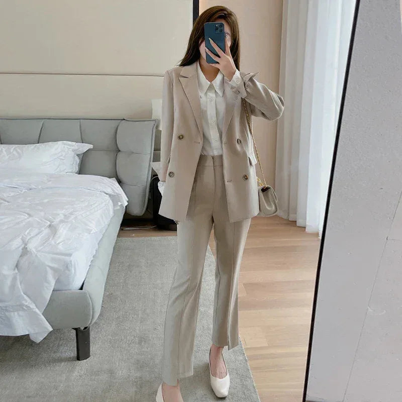 Person taking a mirror selfie wearing a beige suit in a bedroom.