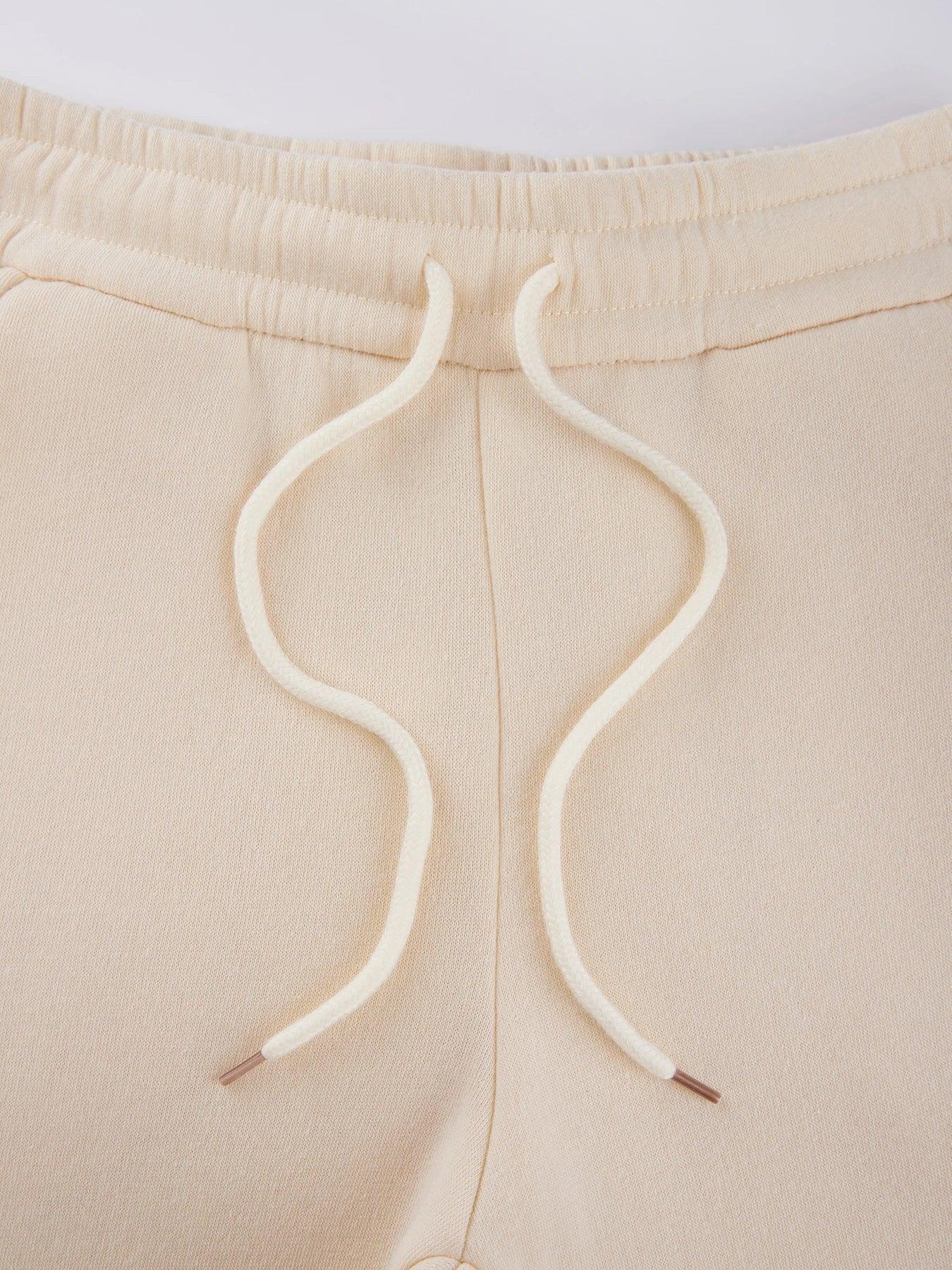 Close-up of beige sweatpants with white drawstrings on a light background