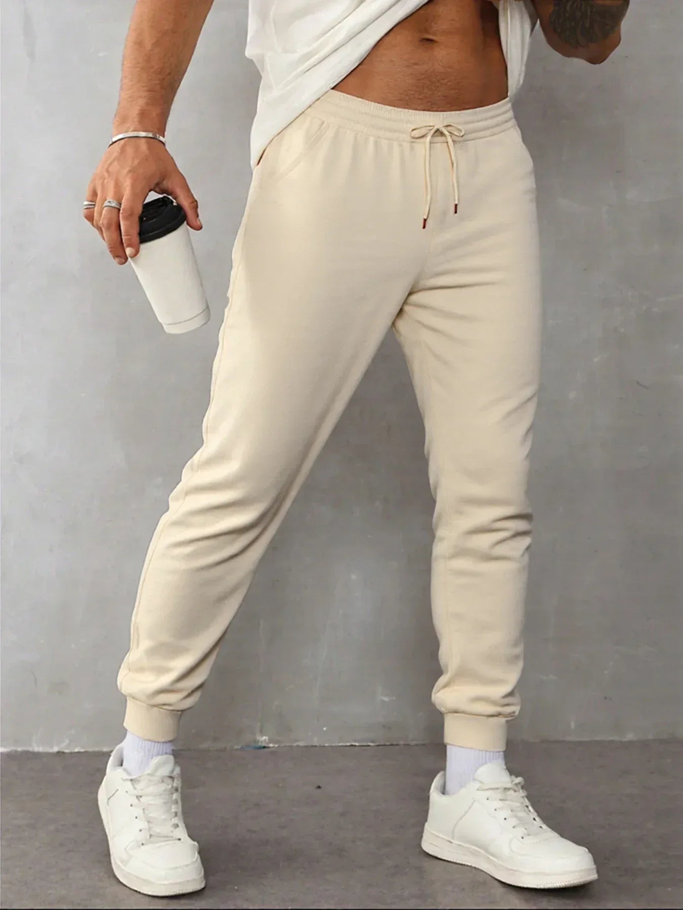 Person wearing beige sweatpants and white sneakers against a gray background