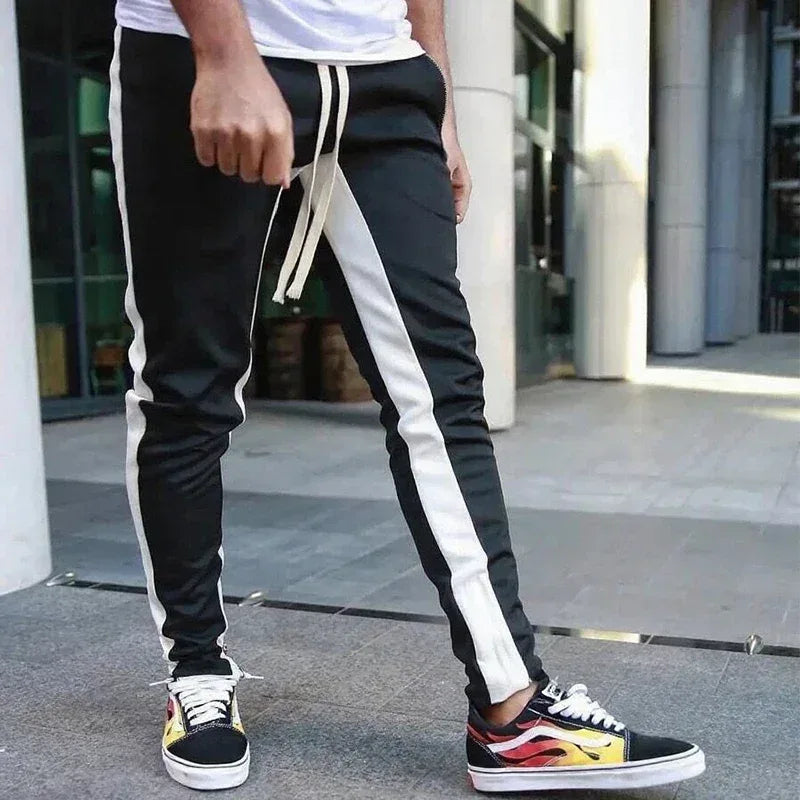 Person wearing black and white track pants with colorful sneakers on a city street.