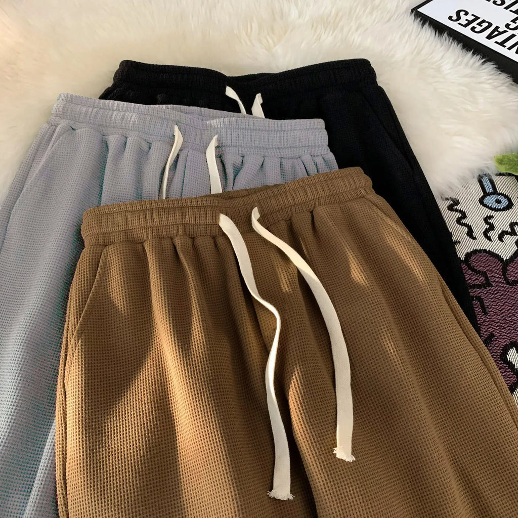 Three pairs of waffle textured pants in brown, gray, and black on a white surface.