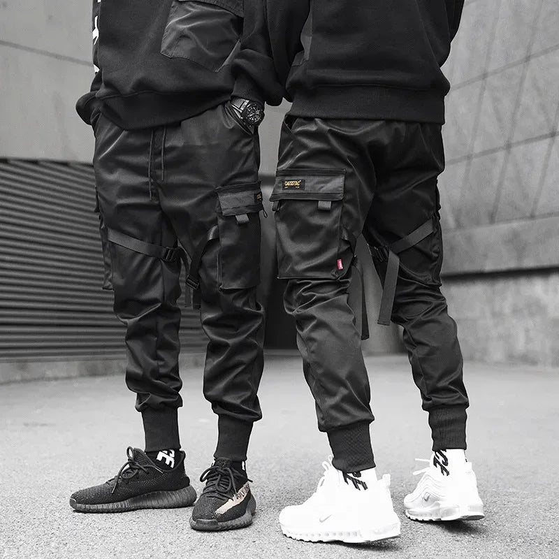 Two people wearing black cargo pants and sneakers standing on a street.