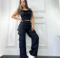 Woman wearing a black outfit with cargo pants against a white wall.