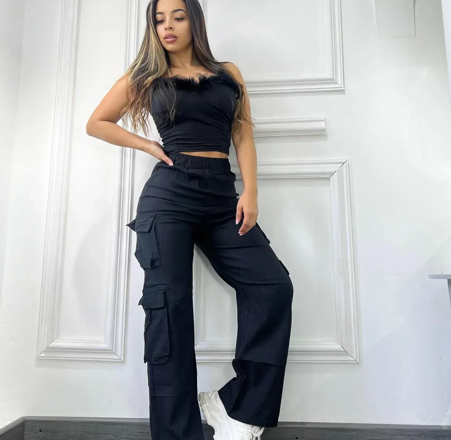 Woman wearing a black outfit with cargo pants against a white wall.