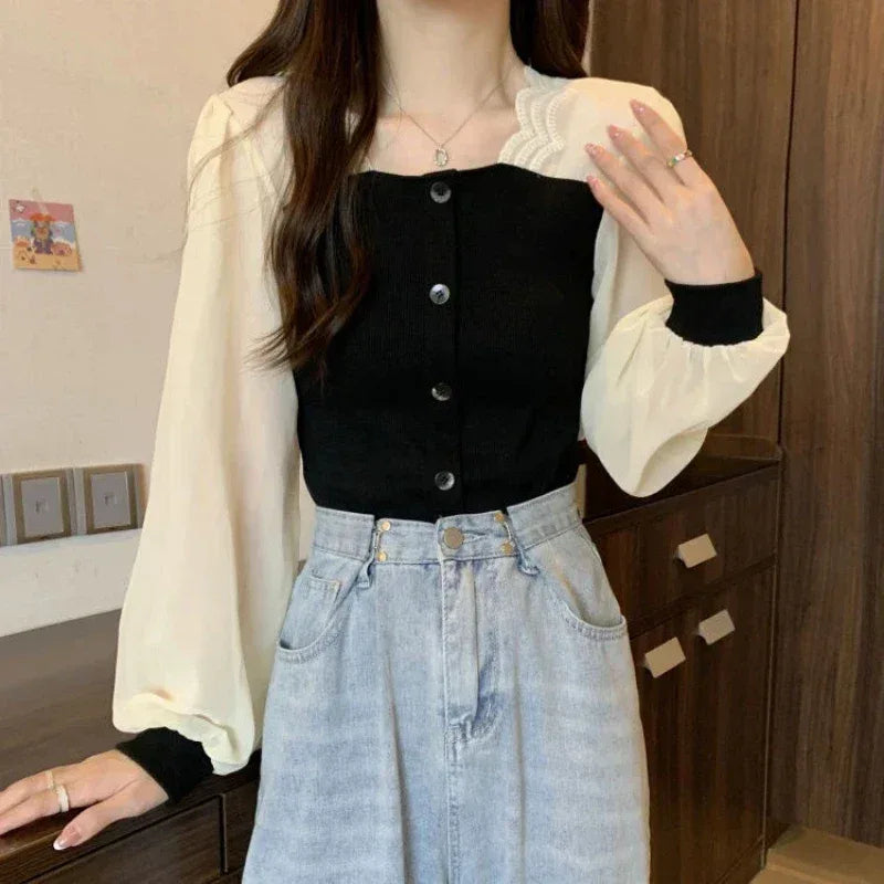 Person wearing a black button-up top, white shirt, and blue jeans indoors.