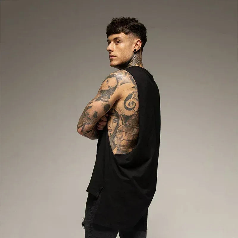 Man with tattoos on his arms and back wearing a black outfit against a gray background