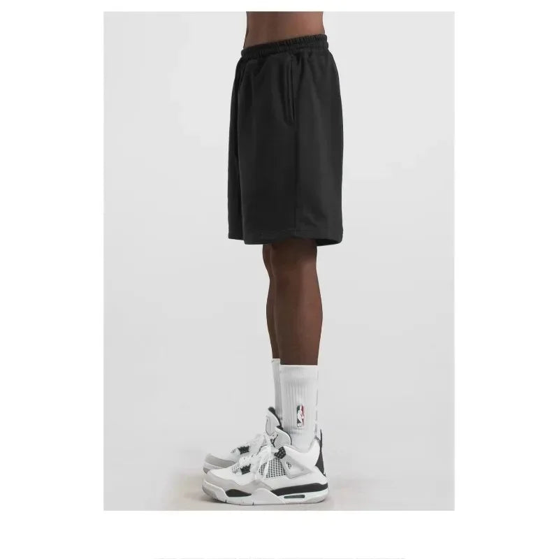 Person wearing black shorts and white sneakers with a logo on a white background