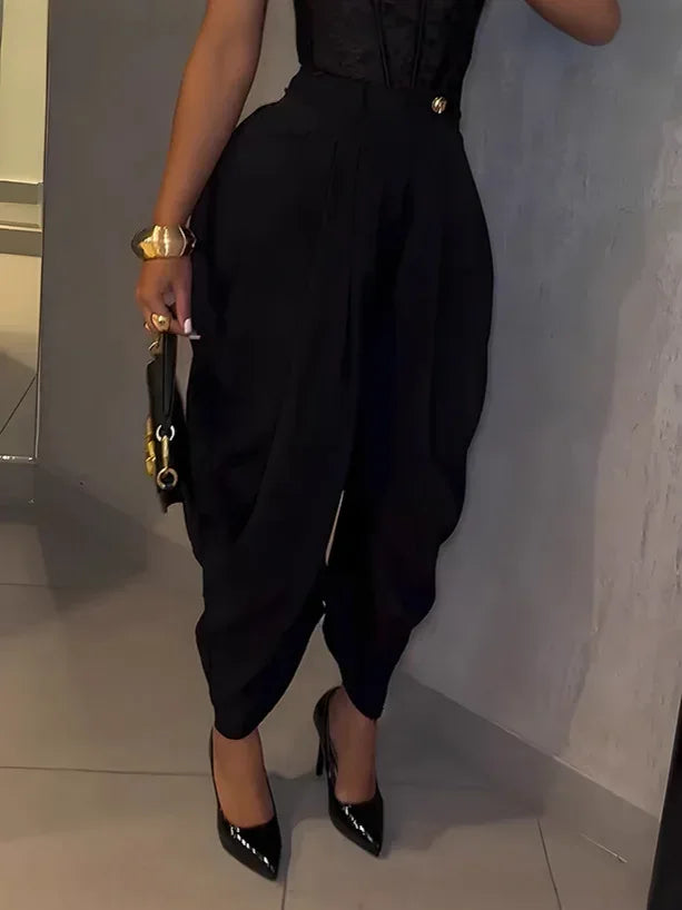 Person wearing a black outfit with high-waisted pants and black shoes, holding a black handbag.