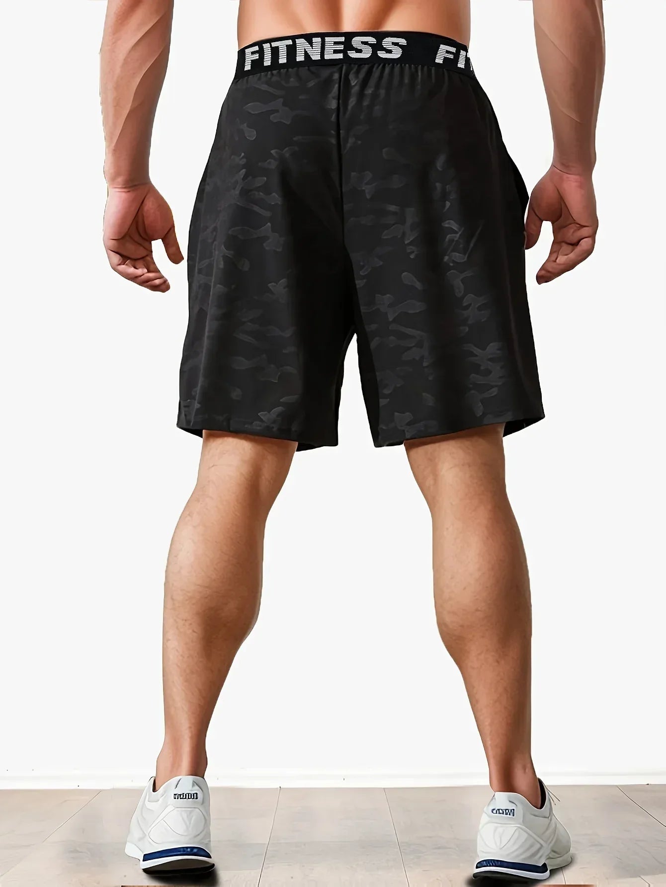Person wearing black camouflage shorts with 'Fitness' waistband on a white background
