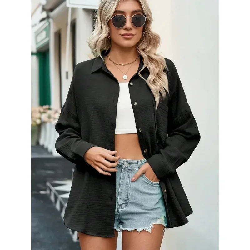 Woman wearing a black shirt over a white crop top and denim shorts, standing outdoors.