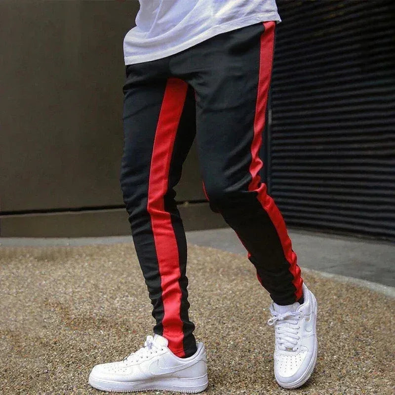 Black and red striped pants with white sneakers on a textured surface.