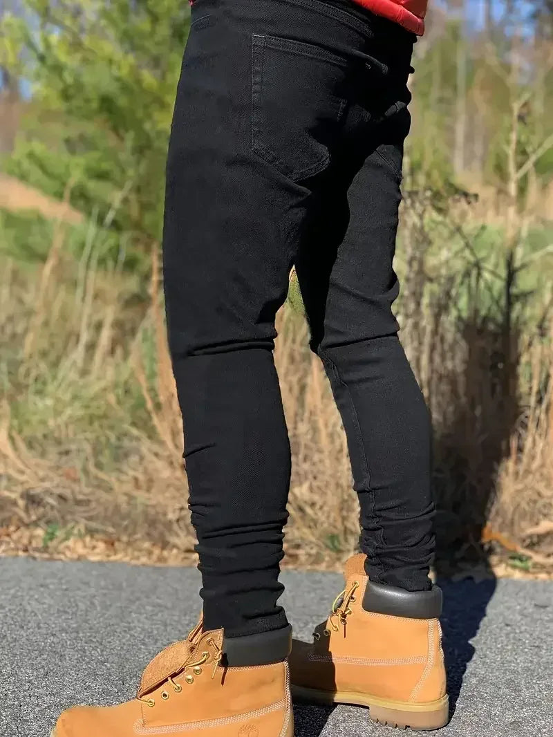 Person wearing black pants and brown boots standing on a road with a natural background