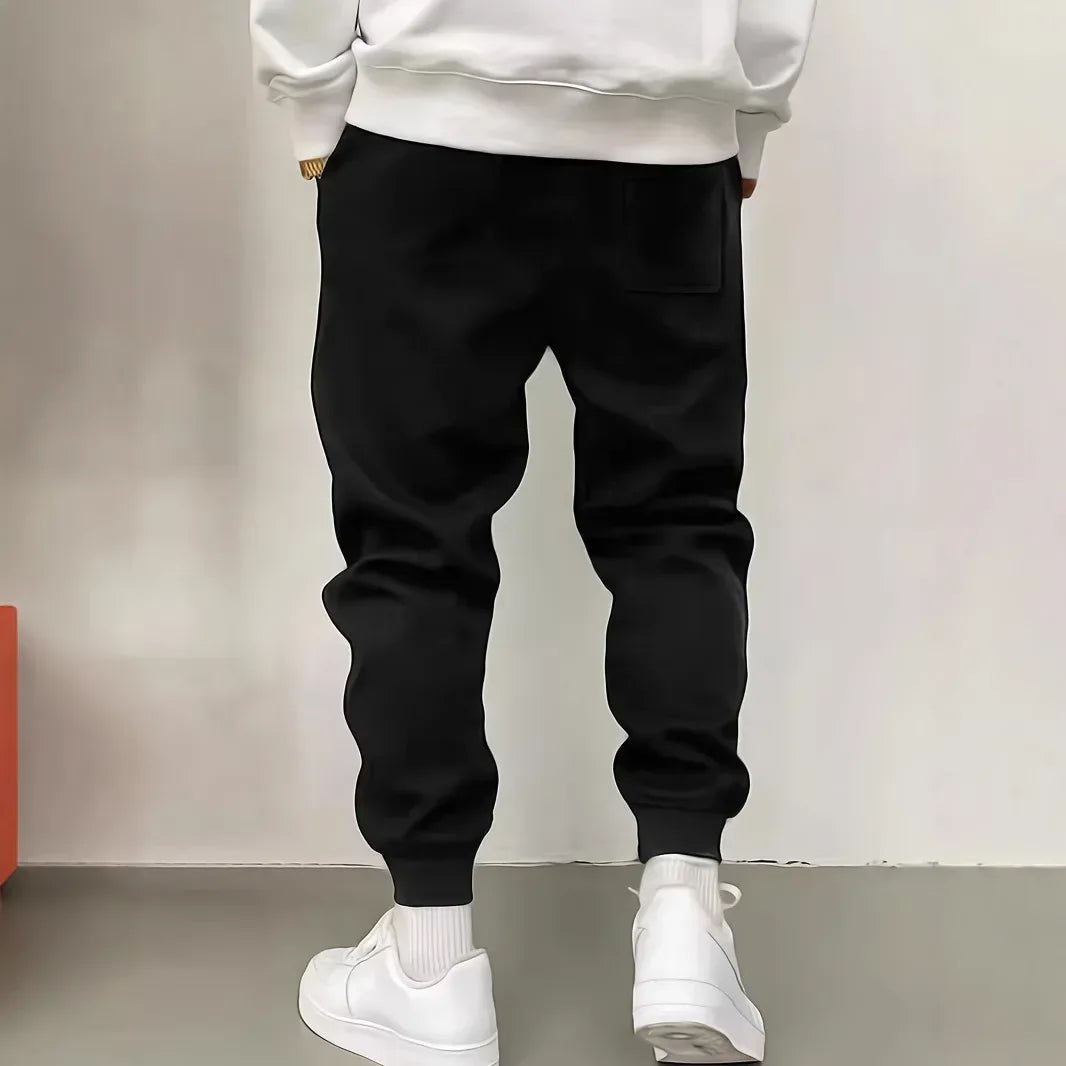 Person wearing black jogger pants and white sneakers on a plain background