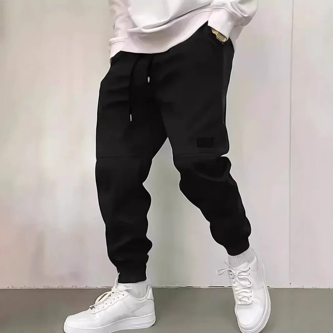 Person wearing black jogger pants and white sneakers on a plain background