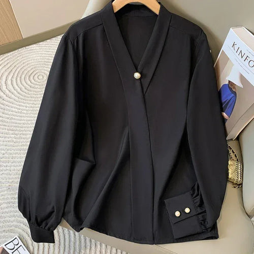 Black blouse with pearl buttons on a hanger against a neutral background