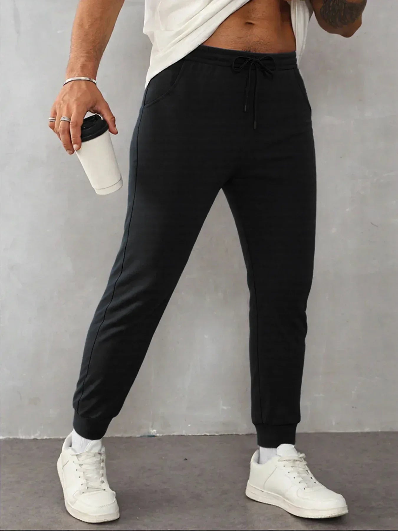 Person wearing black jogger pants and white sneakers against a gray background