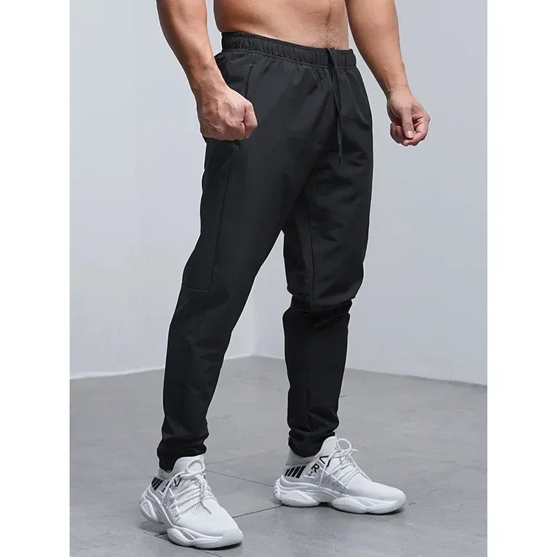 Person wearing black jogger pants and white sneakers on a plain background