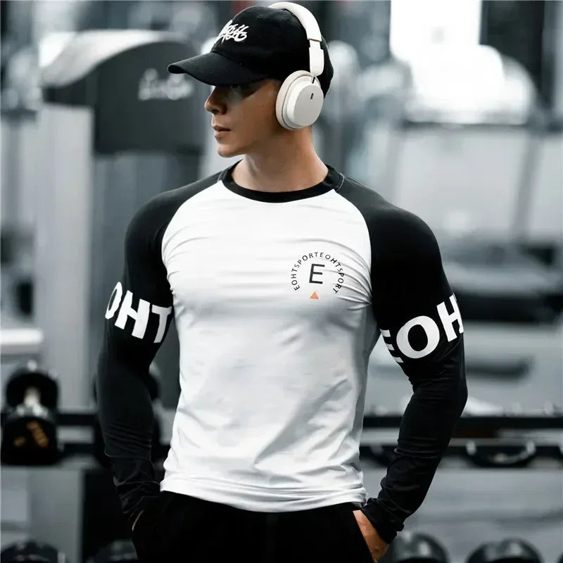 Person wearing a black and white long-sleeve shirt with text, black cap, and headphones in an urban setting.
