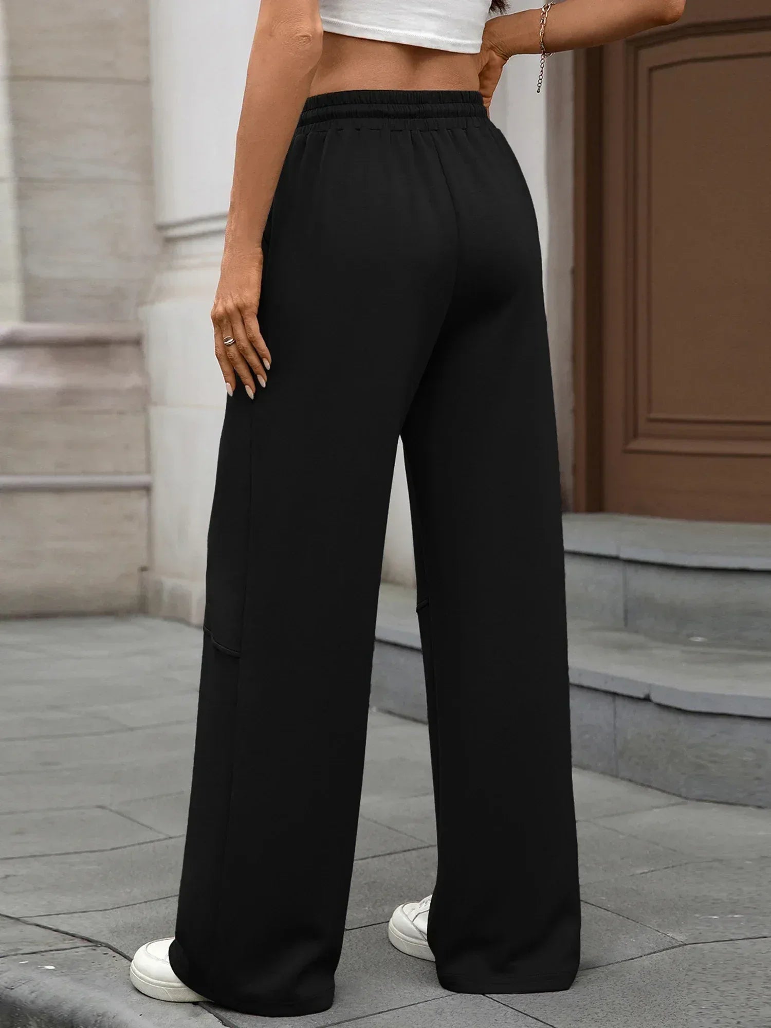 Person wearing black wide-leg pants standing on a sidewalk.
