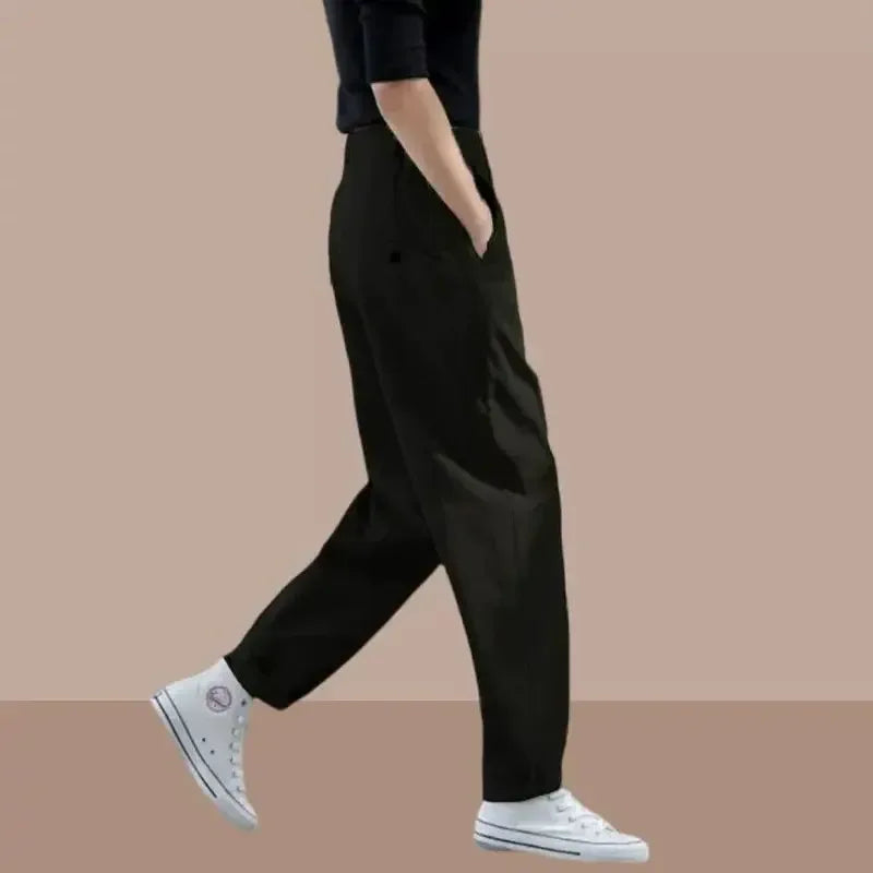 Person wearing black pants and white sneakers on a beige background