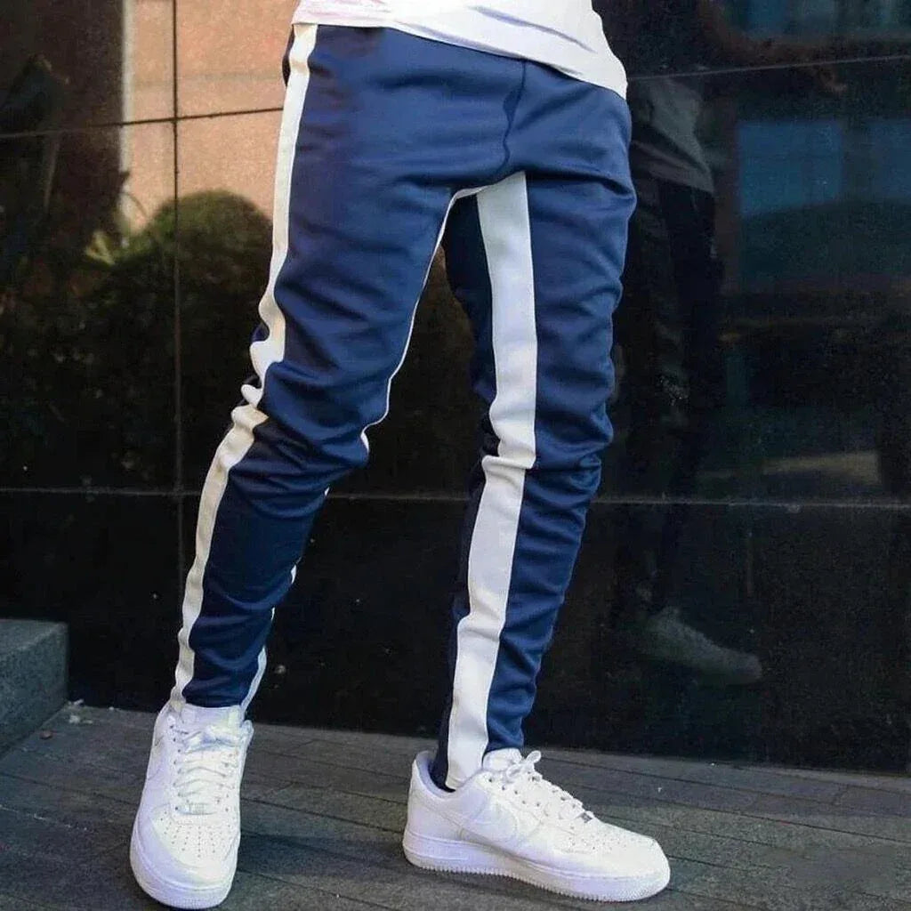 Blue jogger pants with white stripes worn by a person, standing on a wooden floor.
