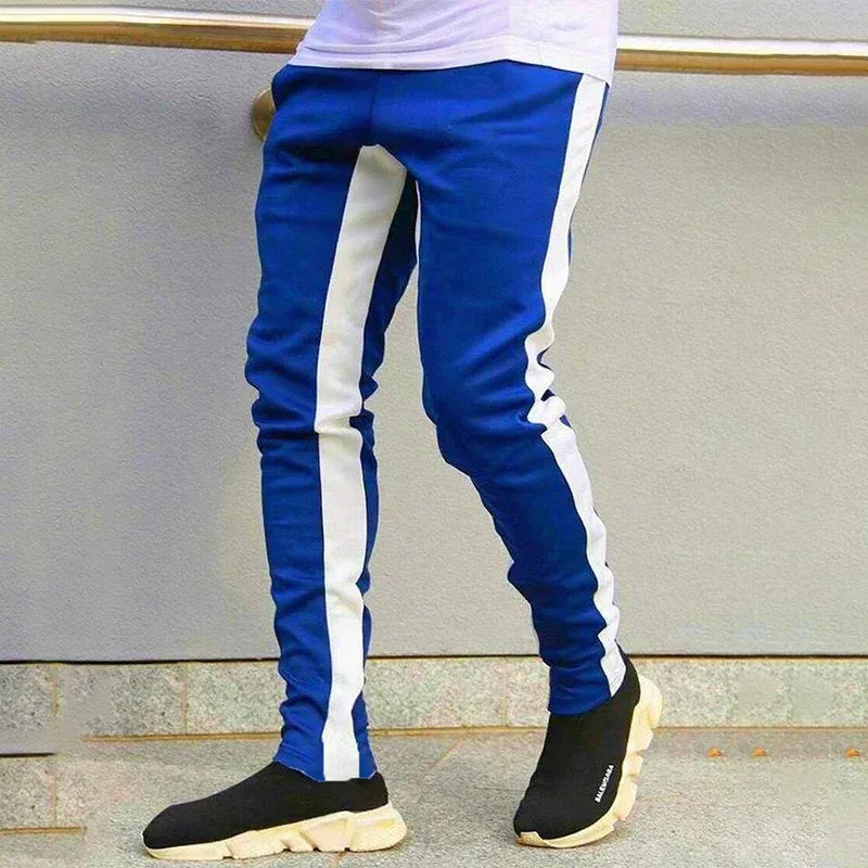 Blue track pants with white stripes worn by a person, standing against a neutral background.