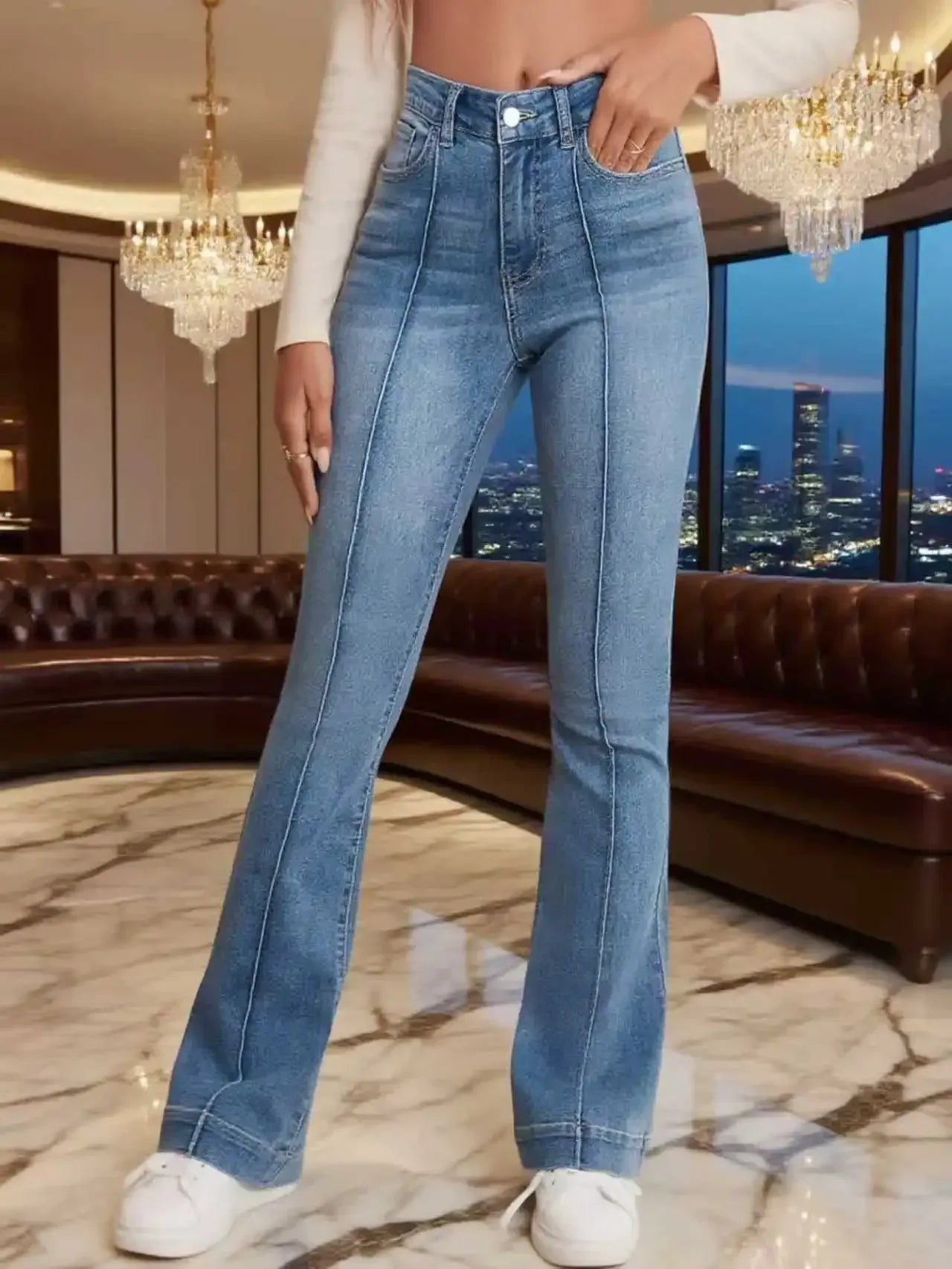 Person wearing blue jeans in a luxurious room with chandeliers and a cityscape view.