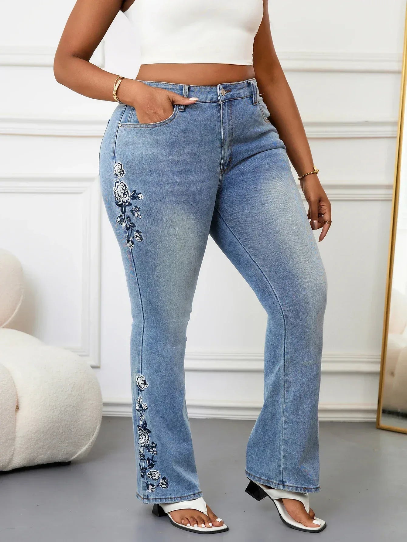 Person wearing blue jeans with floral embroidery on a neutral background