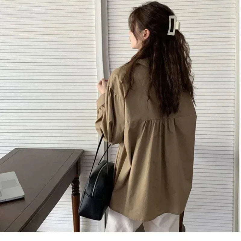 Person wearing a beige shirt and holding a black bag in front of a window.