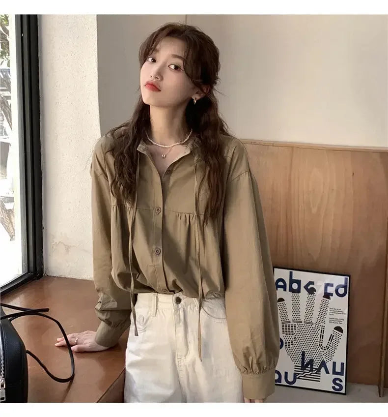 Woman wearing a beige blouse and white pants in a room with a wooden wall and decorative poster.