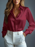 Woman wearing a burgundy satin shirt and white pants against a gray background