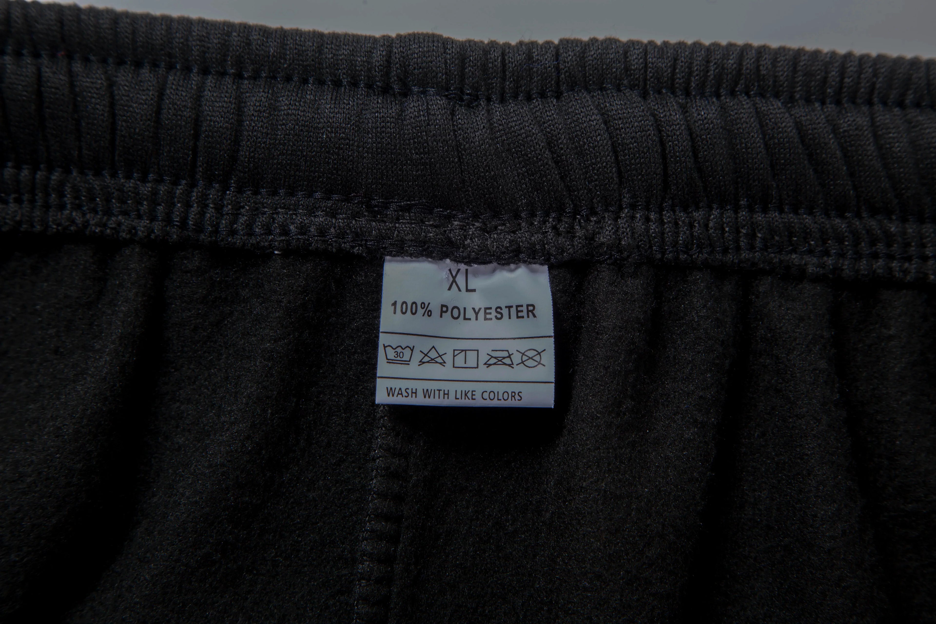 Close-up of a black garment with a label indicating size XL and material 100% polyester.