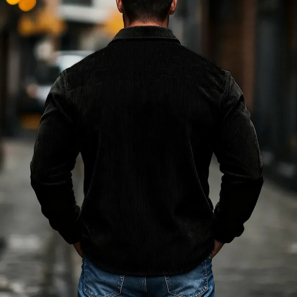 Person wearing a black jacket and blue jeans standing on a street.