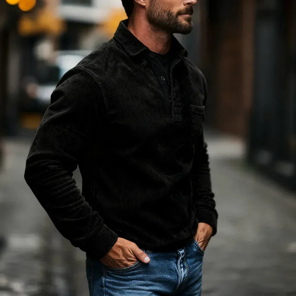 Man wearing a black jacket and blue jeans standing on a street.