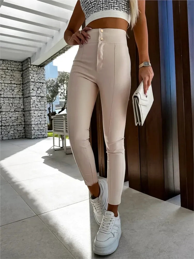 Person wearing beige high-waisted pants with a button detail, white sneakers, and a white clutch outdoors.