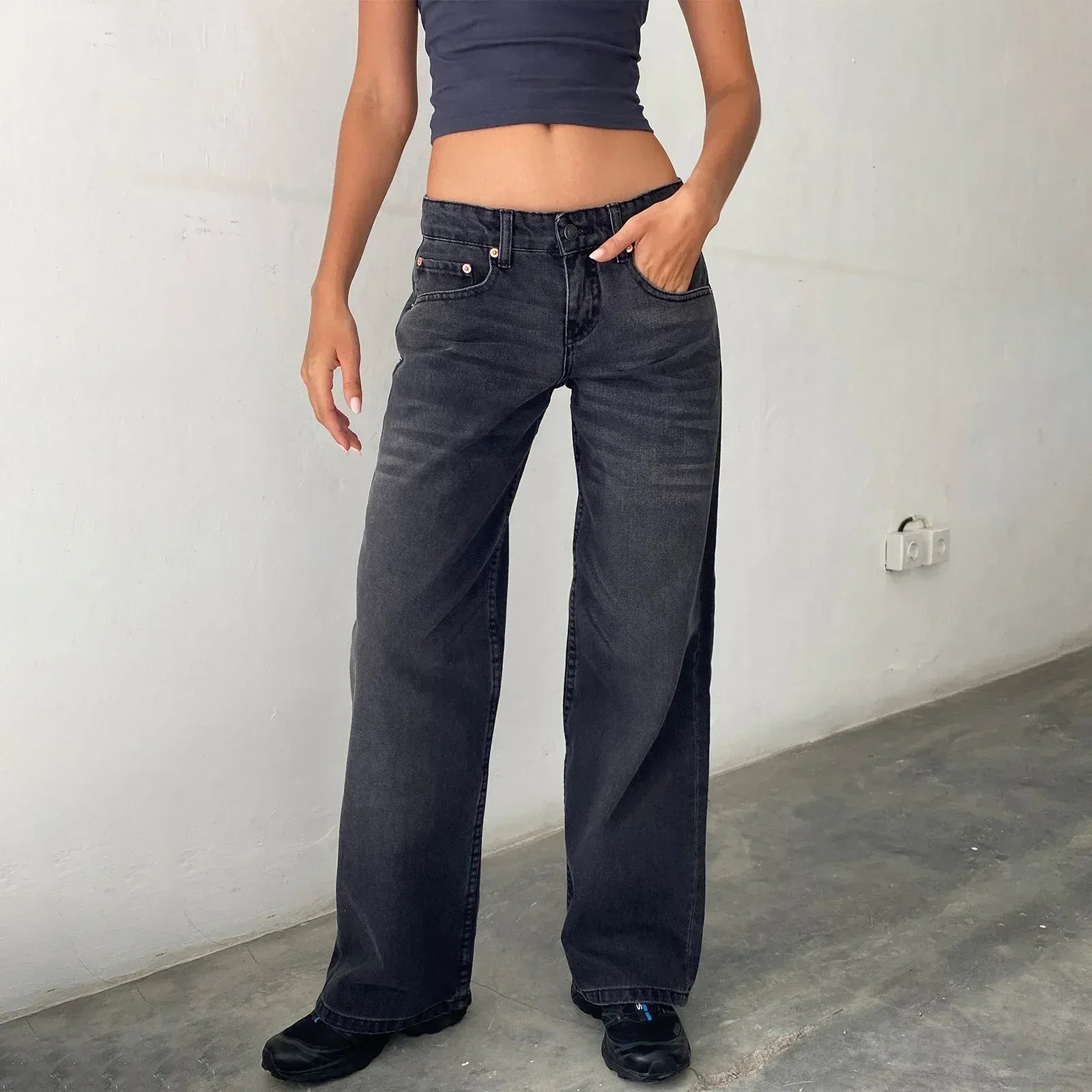 Person wearing dark blue jeans and a cropped top against a plain wall.