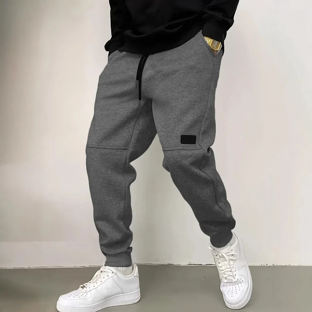 Person wearing gray jogger pants and white sneakers against a plain background
