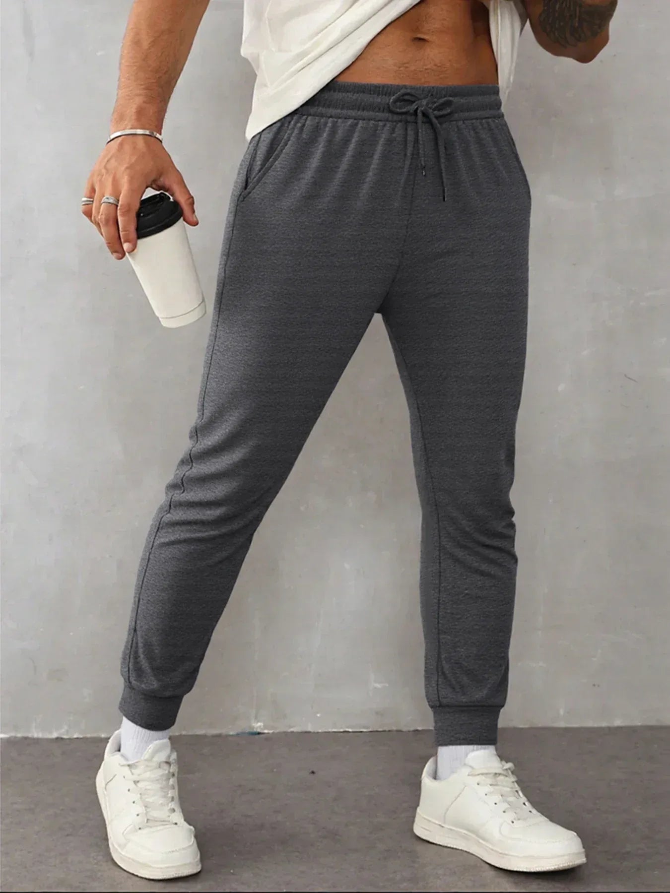 Person wearing gray jogger pants and white sneakers against a plain background