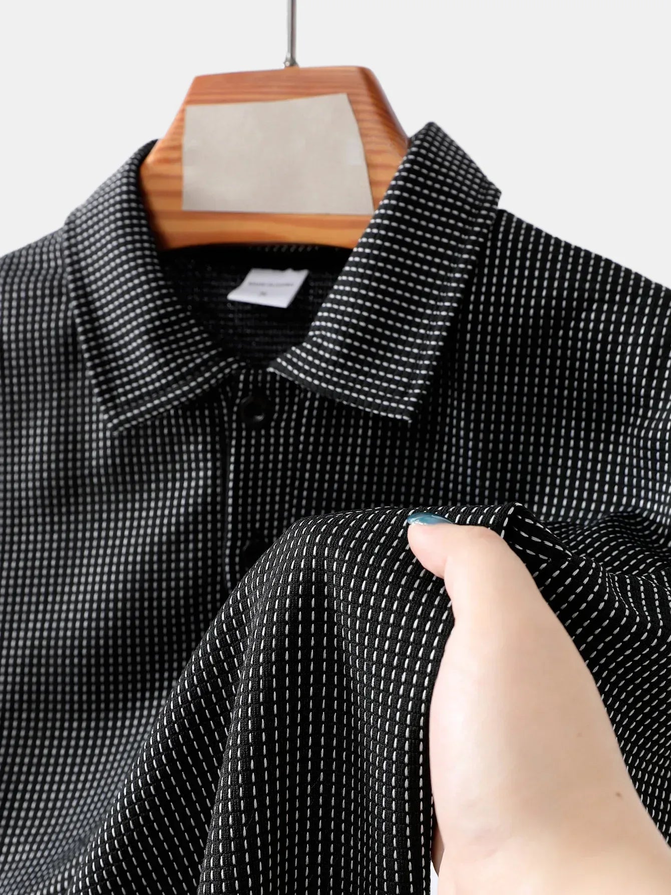 Black and white checkered shirt on a hanger with a hand touching the fabric.