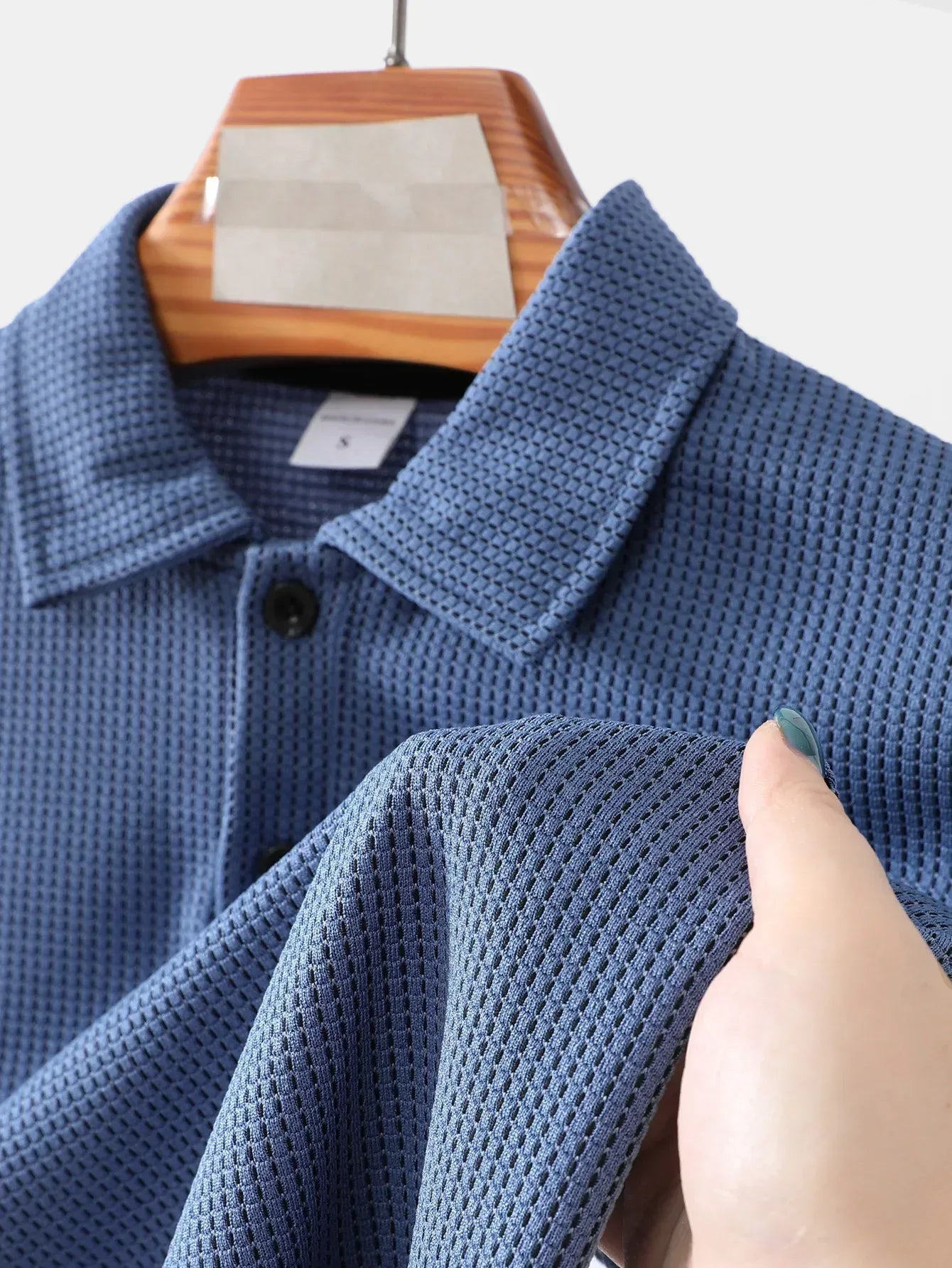 Blue textured shirt on a hanger with a hand touching the fabric