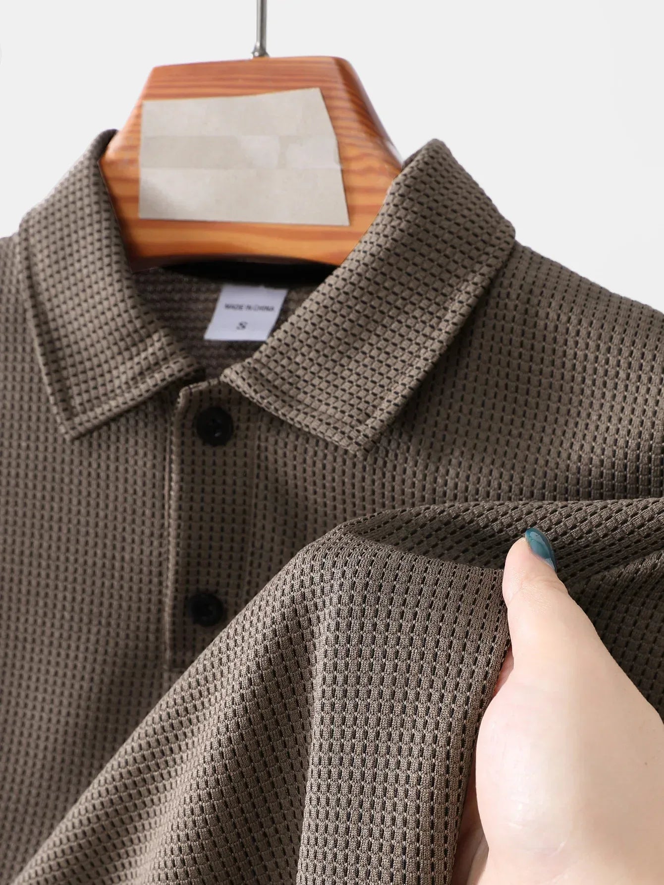 Brown textured jacket on a hanger with a hand touching the fabric