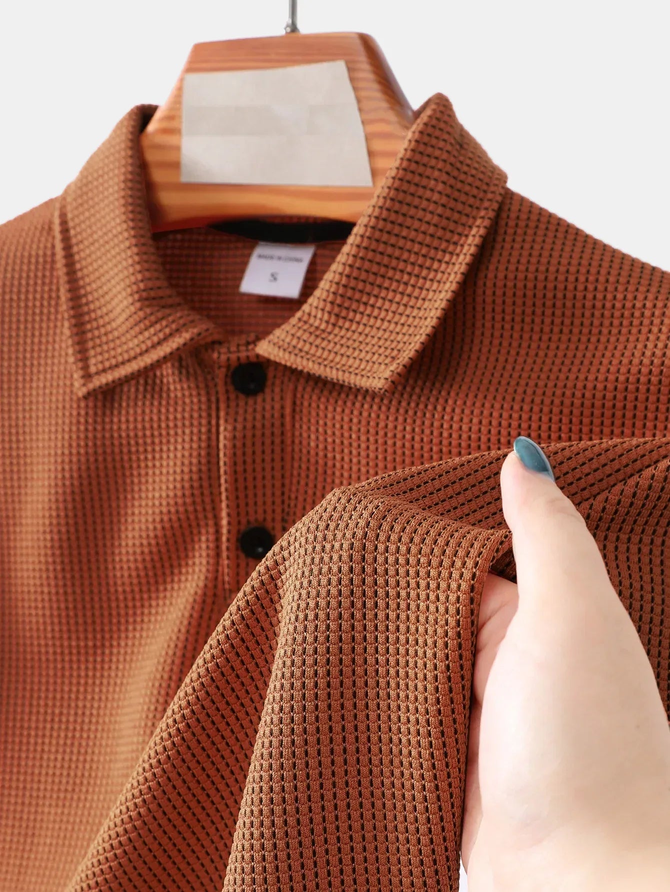 Brown textured shirt on a hanger with a hand touching the fabric.
