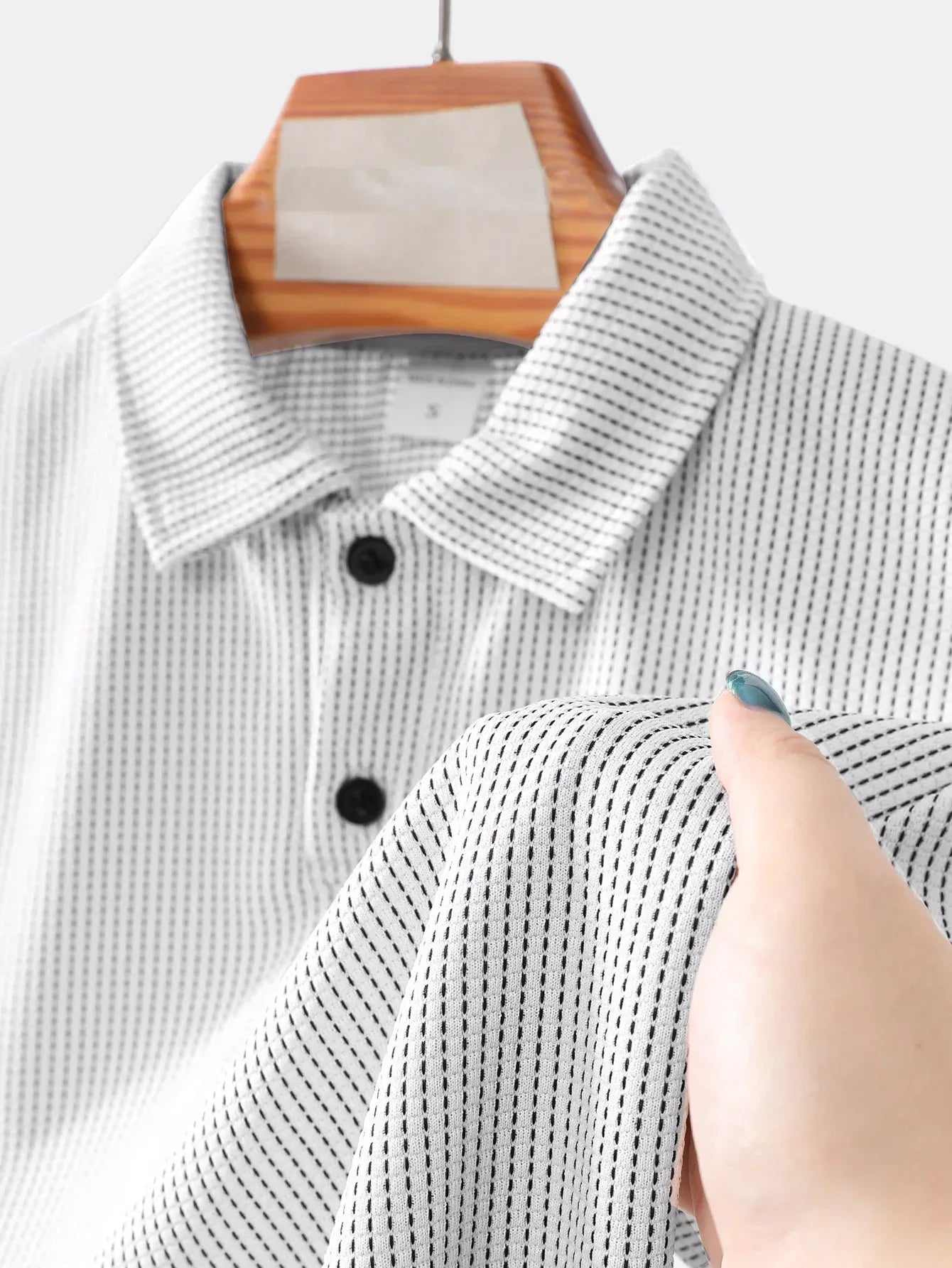 Close-up of a gray and white checkered shirt on a hanger with a hand touching the fabric.
