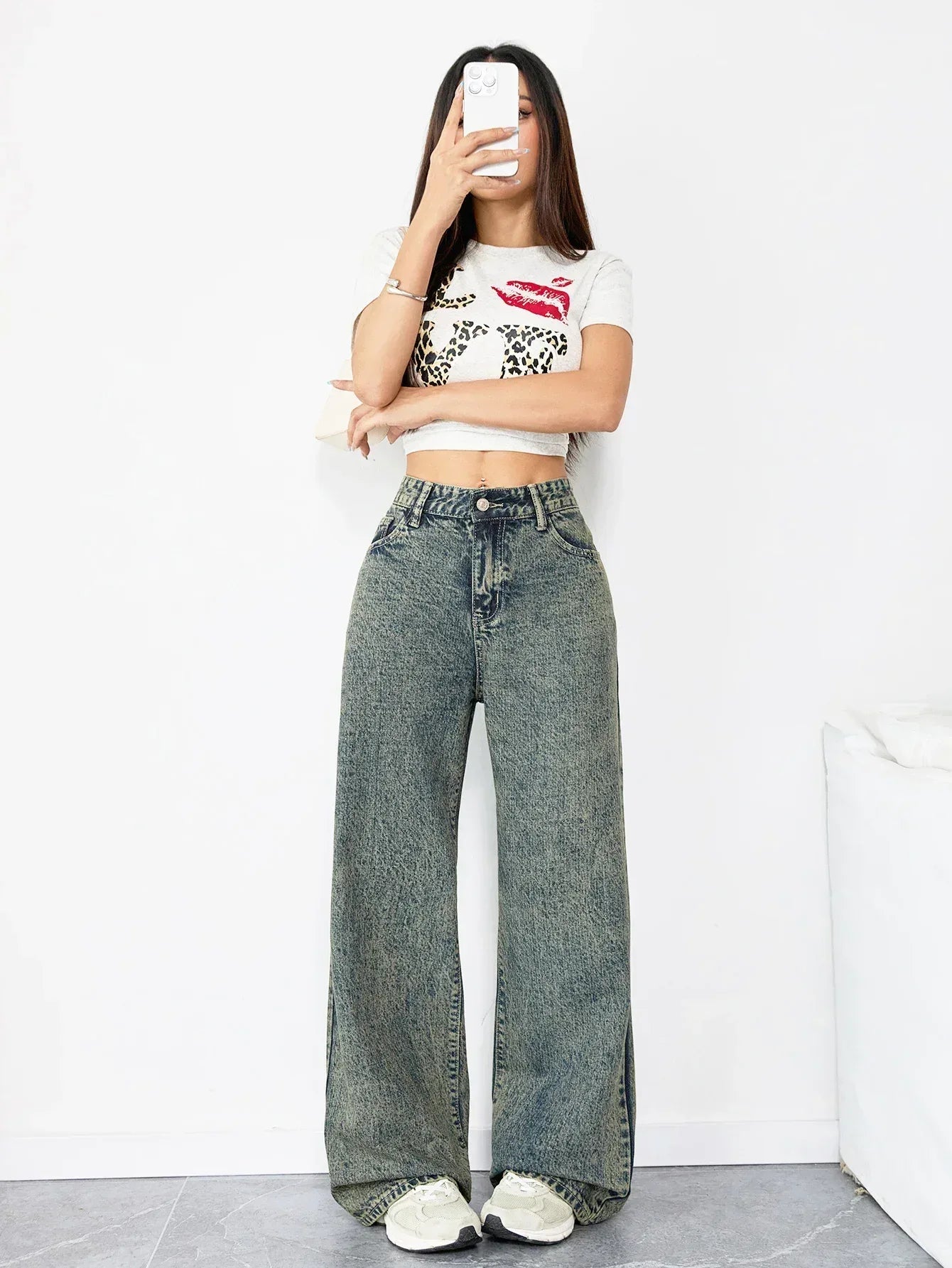 Person wearing a white crop top with red graphics and high-waisted blue jeans on a white background